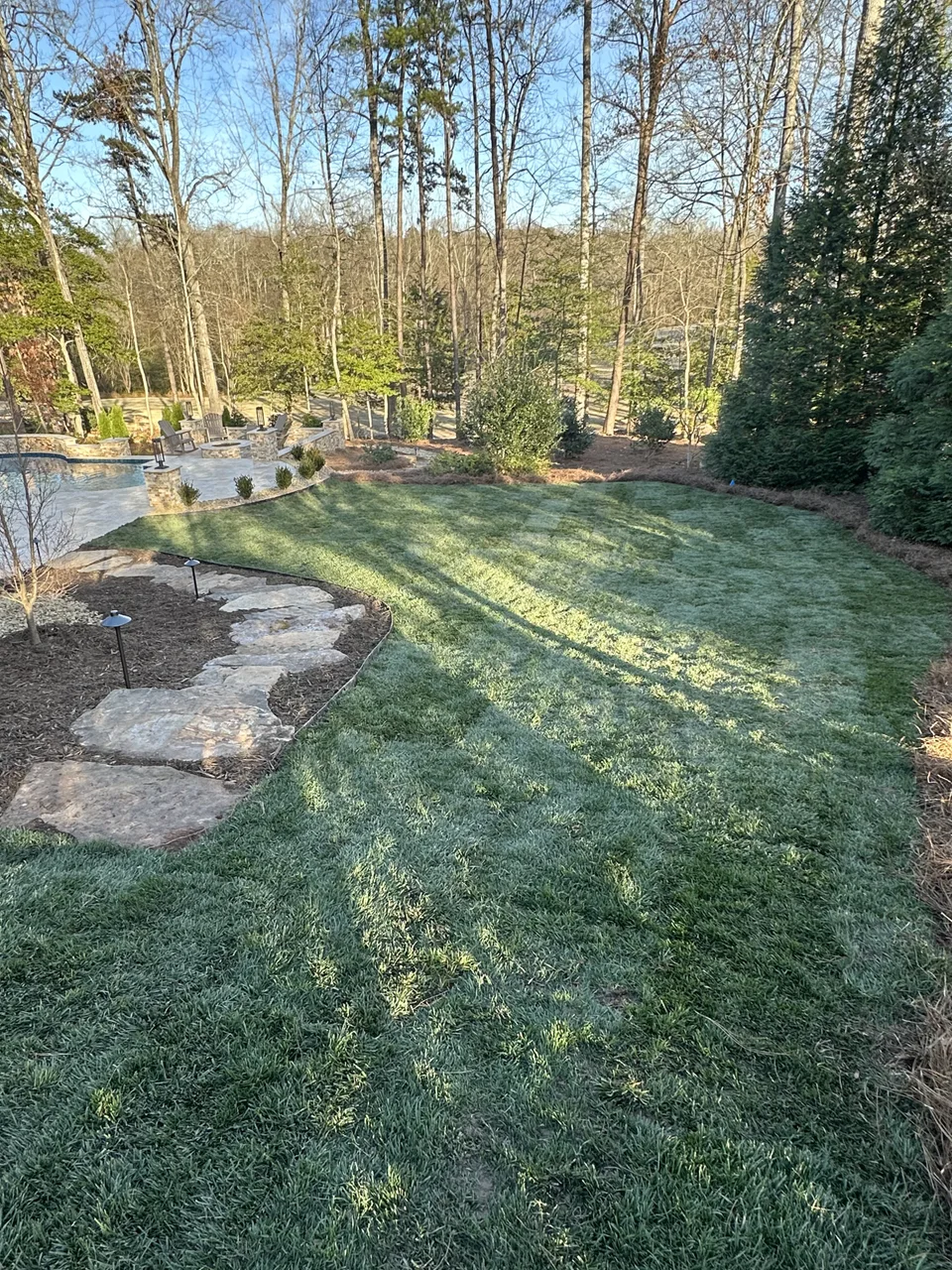 Natural stone steps beside newly laid sod and mulched beds in a wooded backyard